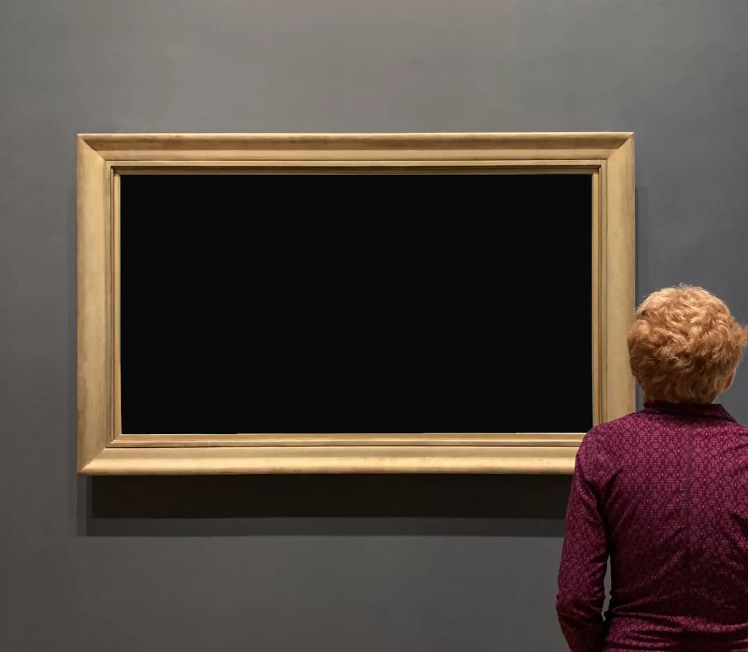 Eine Person steht vor einer leeren, schwarz gerahmten Leinwand an einer grauen Wand in einer Kunstgalerie und denkt über moderne Kunstformen und eine Einführung darin nach, um Kunst zu verstehen.
