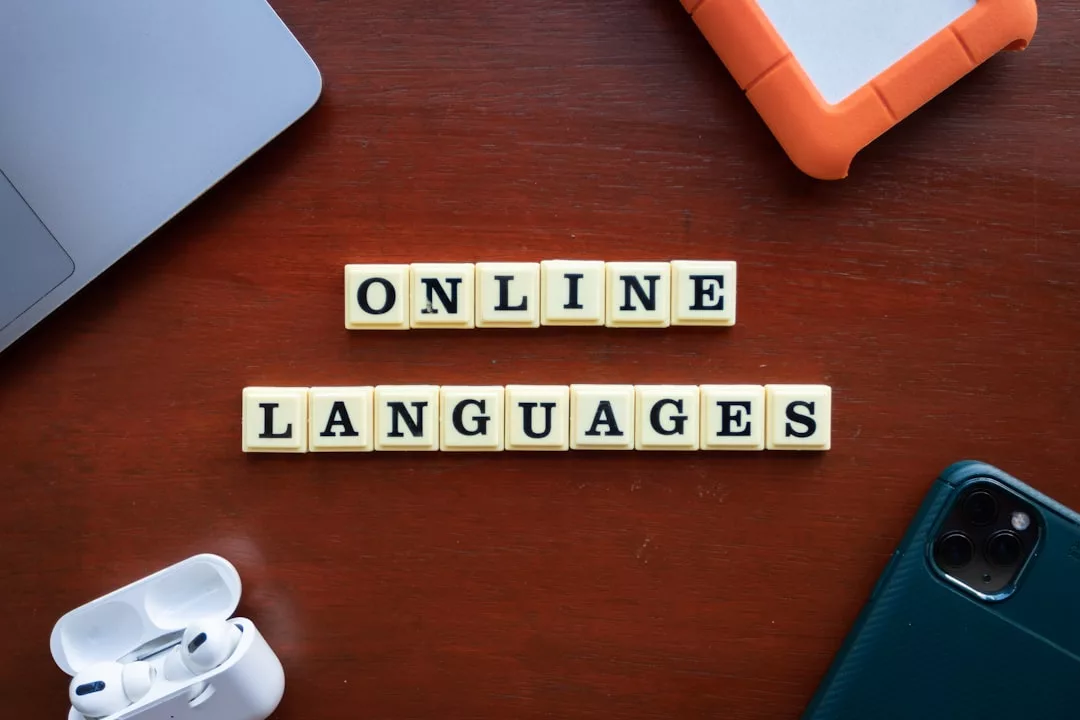 Auf einem Holztisch, umgeben von einem Laptop, einem orangefarbenen externen Laufwerk, kabellosen Kopfhörern und einem Smartphone, stehen Buchstabenkacheln mit der Aufschrift "ONLINE LANGUAGES" - perfekt für effektives Lernen mit Online-Bildungsressourcen.