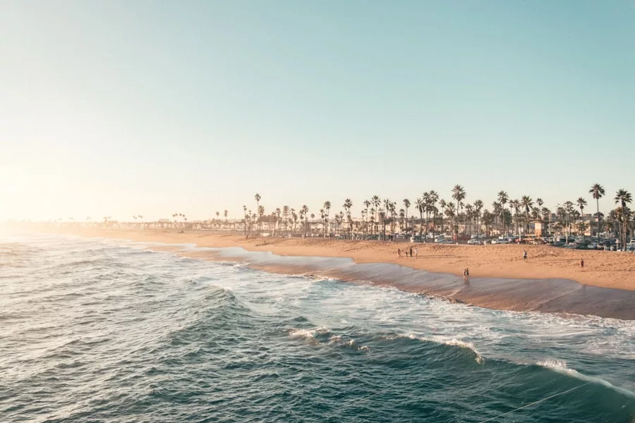 Die Wellen plätschern an einen palmengesäumten Sandstrand unter einem klaren Himmel; die Menschen spazieren am Ufer entlang, genießen persönliches Wachstum und Momente der Besinnung in dieser friedlichen Umgebung.