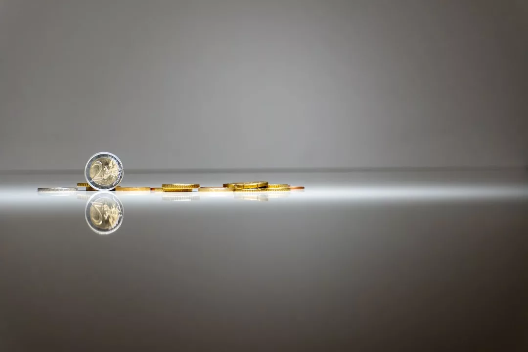 Ein kleiner Stapel und eine einzelne Rolle Münzen sind auf einer reflektierenden Oberfläche vor einem schlichten, hellgrauen Hintergrund platziert und symbolisieren Selbstmotivation und die Bedeutung des Setzens klarer Ziele für das persönliche Wachstum.