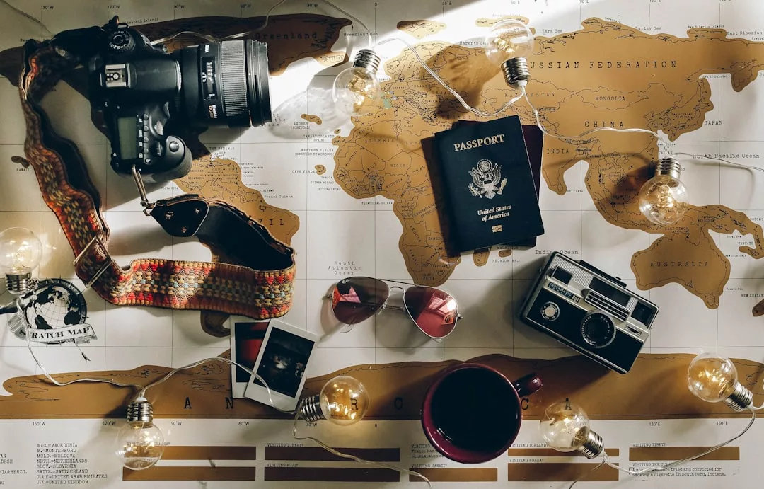 Ein Fotoapparat, ein US-Reisepass, eine Sonnenbrille, alte Fotos, eine Landkarte, eine alte Kamera, eine Tasse und eine Lichterkette auf einer Weltkarte - perfekt für die Reiseplanung und das Sammeln inspirierender Reisetipps.