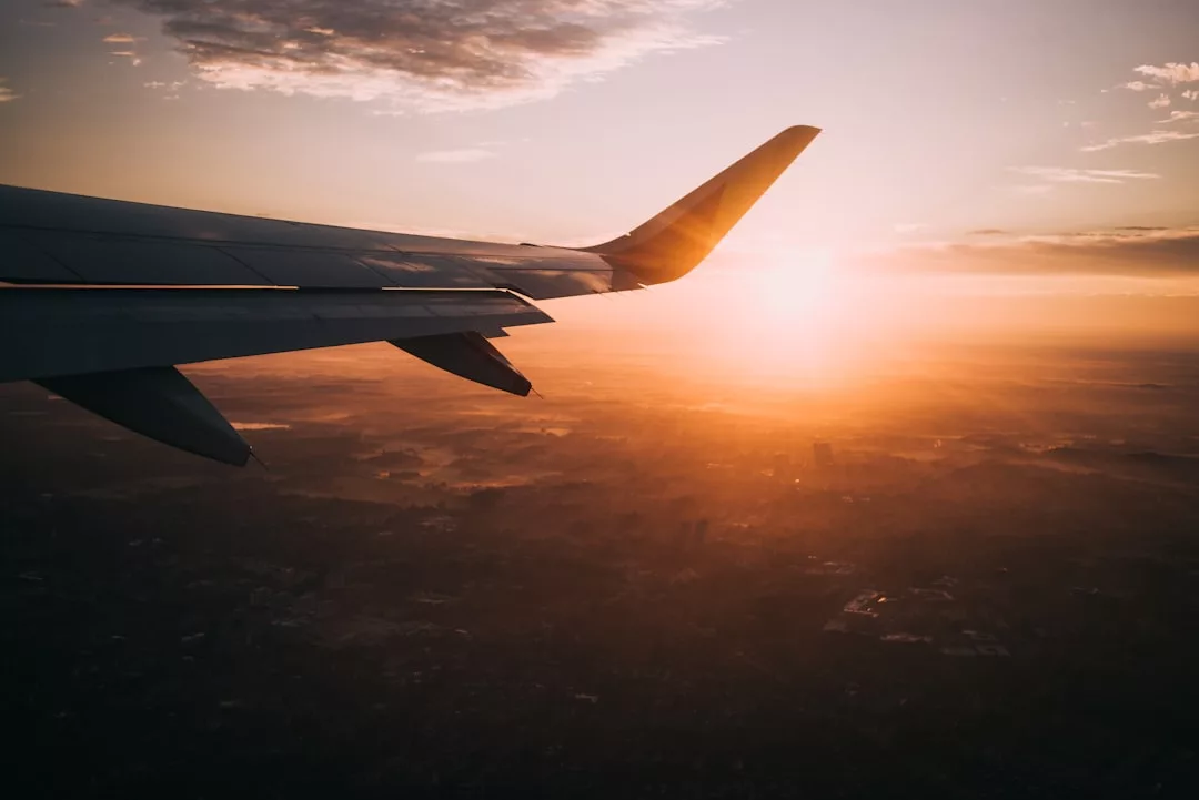 Der Blick aus dem Flugzeugfenster zeigt die Tragfläche und einen leuchtend orangen Sonnenuntergang über der Landschaft - die perfekte Inspiration für Ihre nächste Reiseplanung mit hilfreichen Tipps und Tricks.