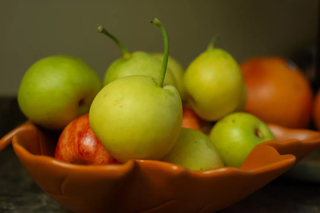 Eine Nahaufnahme einer dekorativen orangefarbenen Schale, gefüllt mit grünen Äpfeln und einem teilweise sichtbaren roten Apfel, auf einer dunklen Fläche - die perfekte Inspiration für saisonales Kochen und frische Rezepte für jeden Anlass.