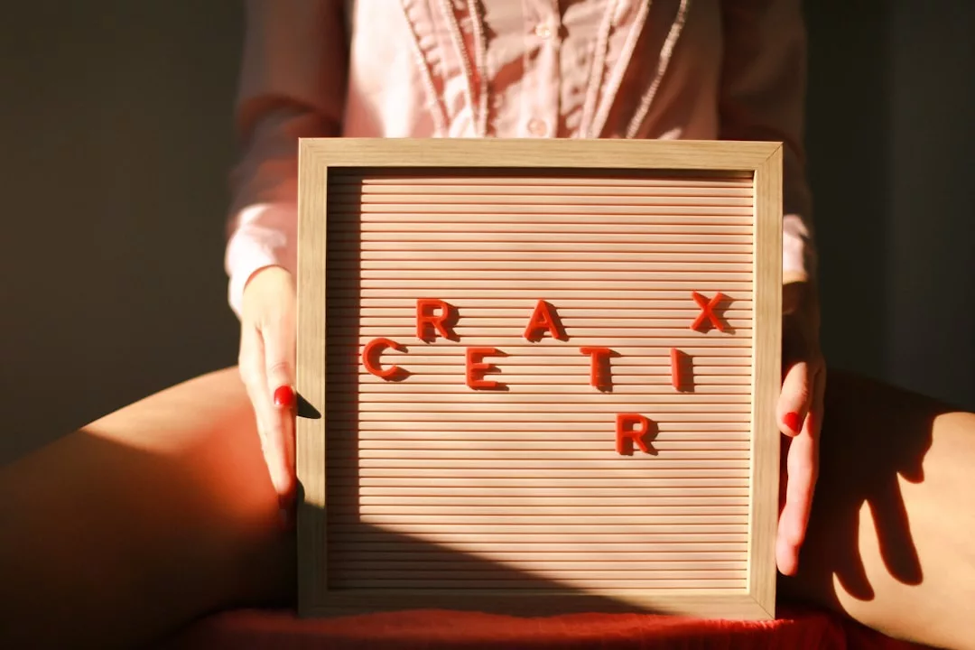 Eine Person in einem rosafarbenen Hemd hält eine Buchstabentafel auf dem Schoß, auf der rote Buchstaben verstreut sind, die "CRAX CETIR" buchstabieren - ein spielerischer Moment, der Methoden der persönlichen Weiterentwicklung widerspiegelt.