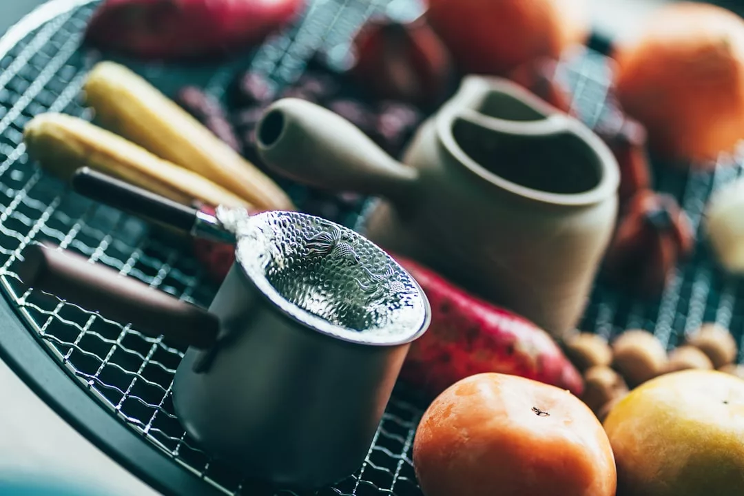 Eine Nahaufnahme eines Grills mit verschiedenen Gemüsesorten, einem kleinen Metallsieb und einer Teekanne aus Keramik auf dem Rost - ideale Küchenutensilien, die man richtig pflegen sollte.
