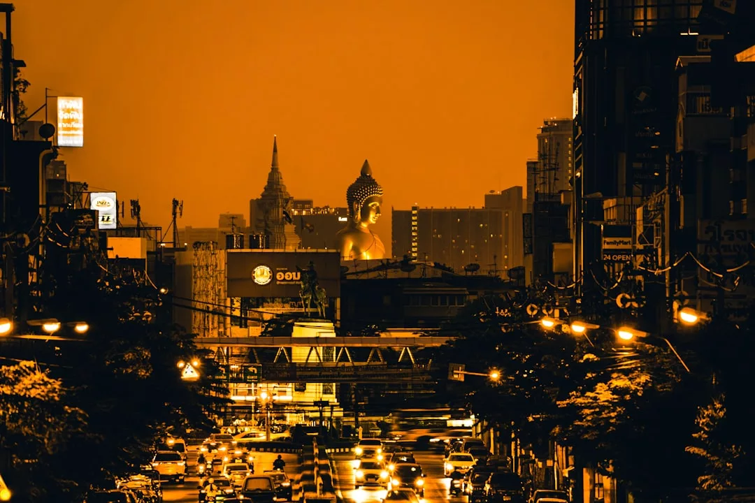 Eine nächtliche Stadtstraße mit starkem Verkehr, beleuchtet von orangefarbenen Lichtern und einer großen Buddha-Statue zwischen Wolkenkratzern - perfekt für alle, die Afrika entdecken wollen, auf einzigartigen Städtereisen Afrika in pulsierenden Metropolen.
