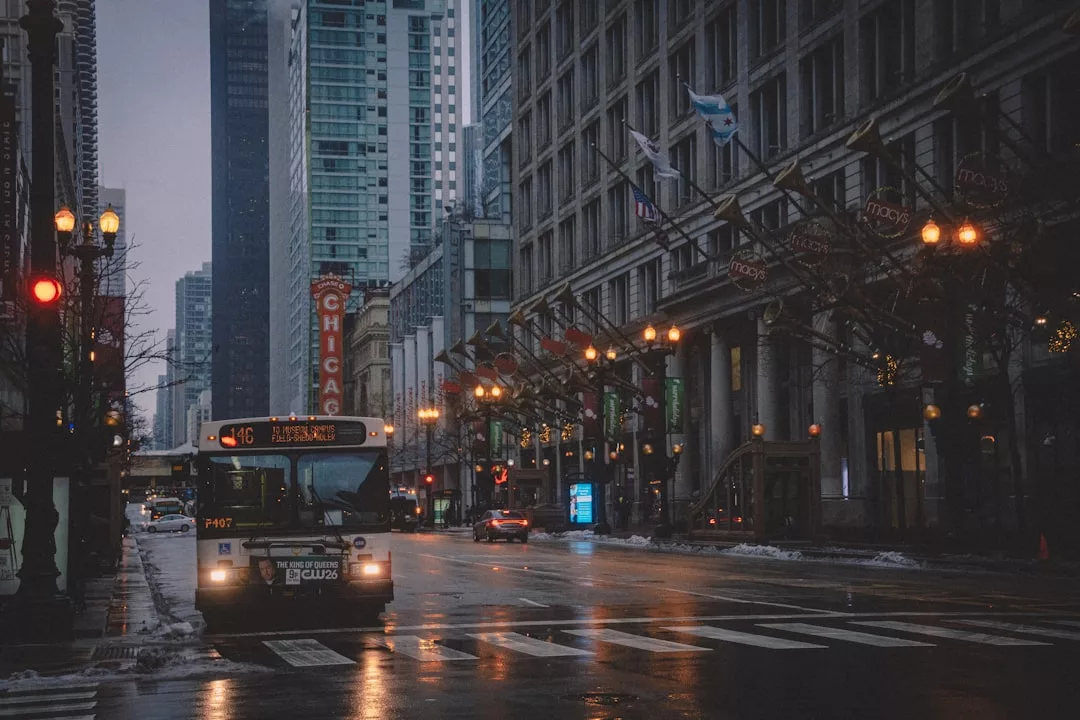Ein Stadtbus der Linie 146 fährt auf einer nassen Straße in Downtown Chicago, einer der großen Metropolen in Amerika, mit hohen Gebäuden und beleuchteten Straßenlaternen am frühen Abend. Perfekt für Liebhaber von Städtereisen Amerika.