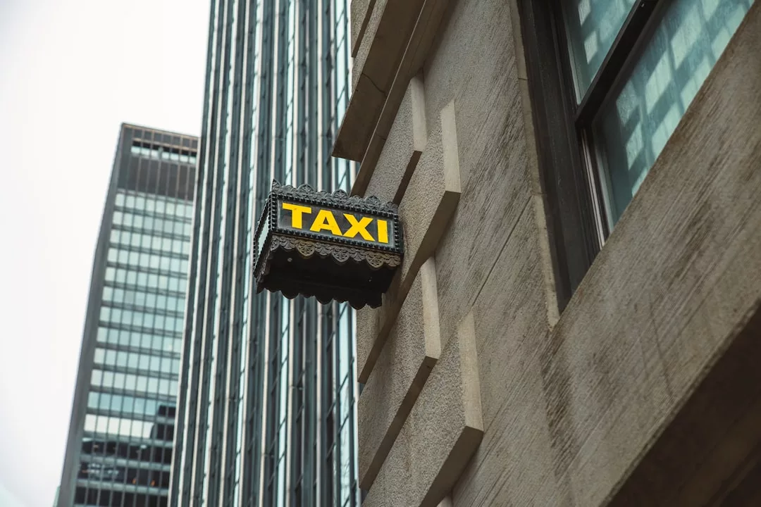 Ein gelb-schwarzes "TAXI"-Schild ist an der Seite eines Gebäudes angebracht, mit hohen gläsernen Bürogebäuden im Hintergrund - ein Hinweis darauf, wo Unternehmen innovative Strategien entwickeln könnten.