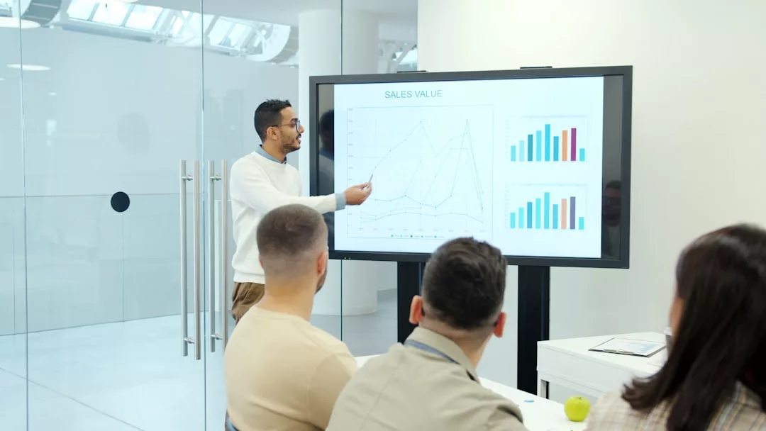 Ein Mann hält einen Vortrag über "Sales Value" anhand von Linien- und Balkendiagrammen und gibt wertvolle Strategien und Tipps zur Entscheidungsfindung mit drei Kollegen in einem modernen Büro.