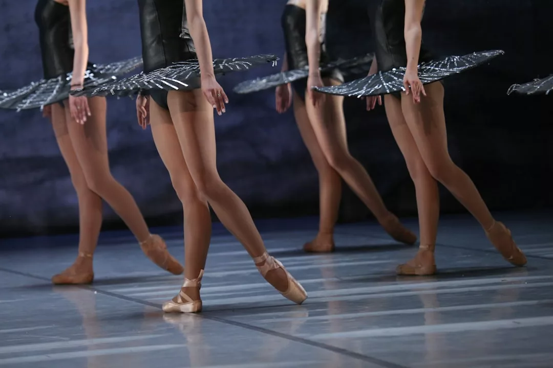 Balletttänzerinnen und Balletttänzer in schwarzen Tutus und Spitzenschuhen stehen in Formation mit ausgestreckten Beinen und Armen an den Seiten auf der Bühne und präsentieren einen eleganten Ausdruck in diesen anmutigen Tanzvorführungen der Kunst.