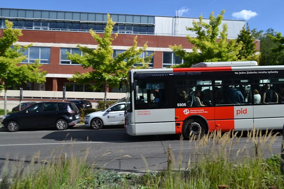 Ein rot-weißer Stadtbus fährt auf einer Straße neben geparkten Autos, mit einem Backsteingebäude und grünen Bäumen im Hintergrund - perfekt, um Networking-Tipps zu entdecken, die helfen, ein starkes Netzwerk aufzubauen.