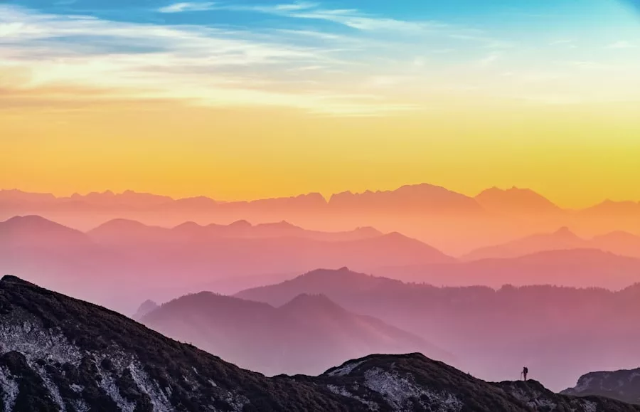 Geschichtete Gebirgszüge bei Sonnenuntergang mit einem farblich abgestuften Himmel; eine einsame Gestalt, vielleicht ein Laufanfänger, der Lauftipps sucht, um richtig zu starten, steht auf einem Grat im Vordergrund.
