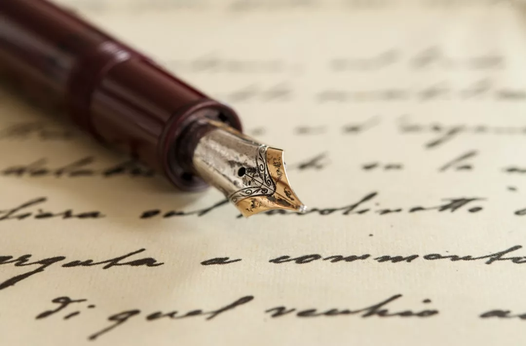 Eine Nahaufnahme eines Füllfederhalters, der auf einem handgeschriebenen, kursiven Text auf Papier ruht, der die Kunst des Schreibens und die Kreativität hinter inspirierenden Kurzgeschichten einfängt.