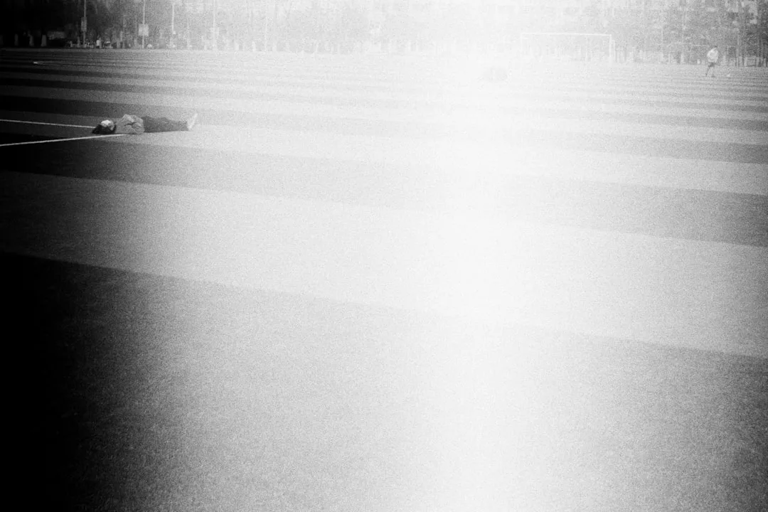 Eine Person liegt auf einem gestreiften Feld, durch dessen Mitte ein helles, überbelichtetes weißes Licht vertikal verläuft. So entsteht ein abstrakter Hintergrund, der Themen wie Behandlung oder Vermeidung suggeriert, als ob man sich der Reisekrankheit stellt oder ihr entkommt.