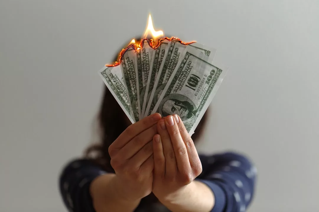 Eine Person hält mehrere brennende 100-US-Dollar-Scheine vor sich, wobei die Flammen den oberen Rand des Geldes erreichen - ein intensives Bild, das fehlende Strategien für finanzielle Notfälle symbolisiert.