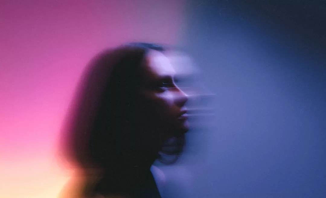 Eine unscharfe Silhouette einer Person mit schulterlangem Haar erscheint vor einem Hintergrund mit Farbverläufen in Rosa-, Lila- und Blautönen und symbolisiert Prävention und Intervention bei Mobbing in der Schule.