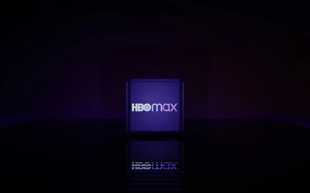 Ein lilafarbener Würfel mit dem HBO Max-Logo steht mittig vor einem dunklen Hintergrund und spiegelt sich auf einer glänzenden Oberfläche darunter - perfekt für Filme und Serien Fans auf der Suche nach neuen Unterhaltungstipps.