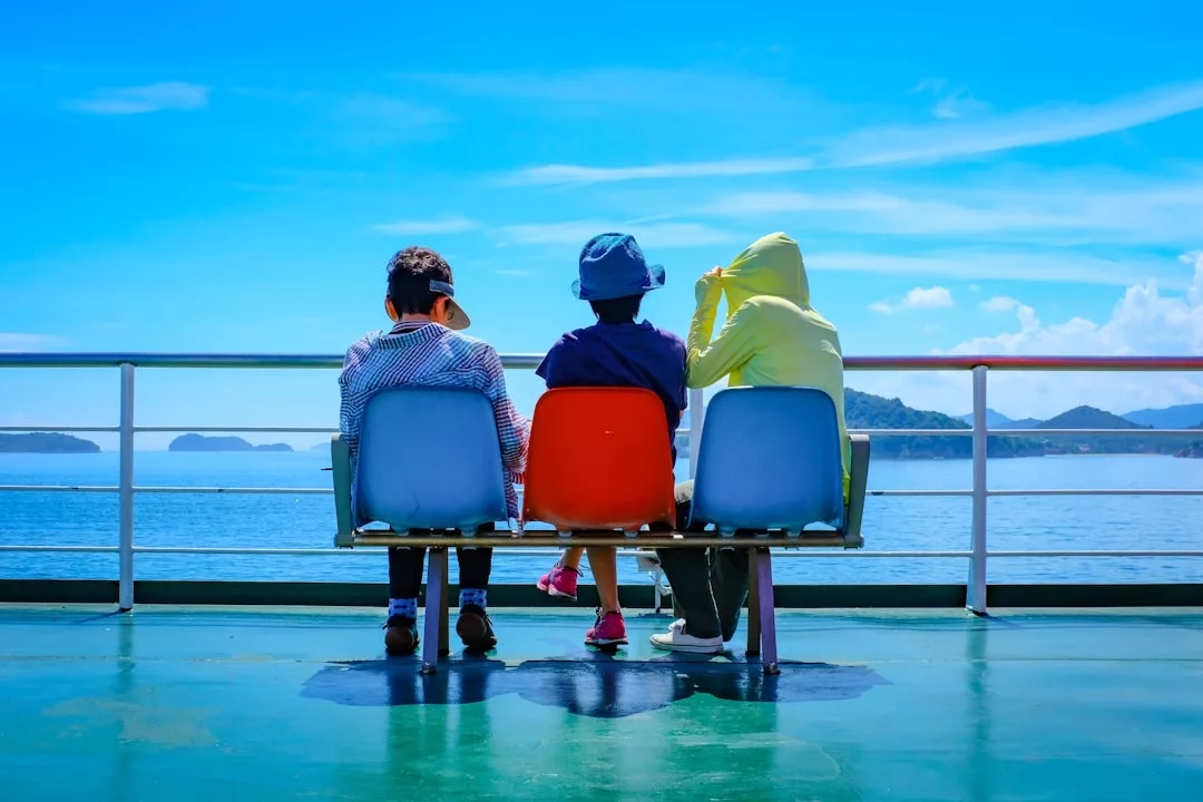 Drei Kinder sitzen auf bunten Stühlen auf einem Fährdeck mit Blick auf das Meer, den blauen Himmel und die fernen Inseln - ein perfekter Moment für Familienurlaub und tolle Urlaubsideen für Familien.