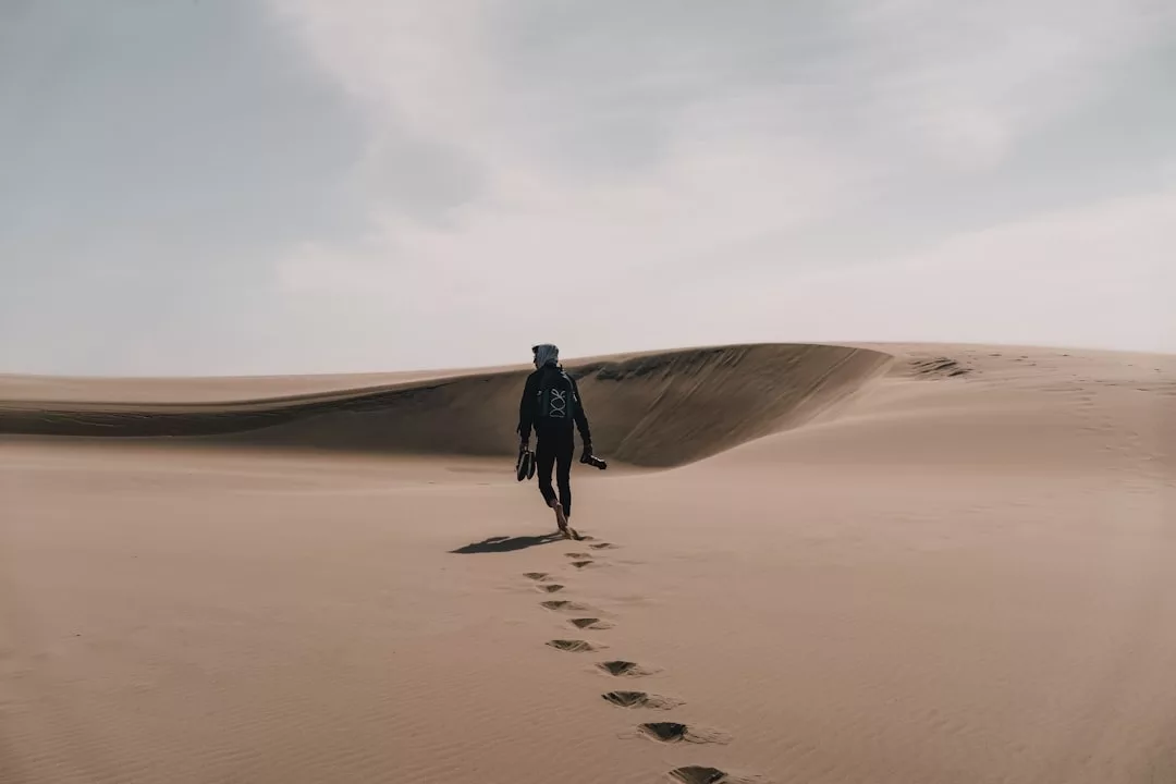 Ein Mensch wandert allein über sandige Dünen und hinterlässt Fußspuren unter einem teilweise bewölkten Himmel - die perfekte Möglichkeit, Natur zu entdecken und unvergessliche Wanderreisen zu erleben.