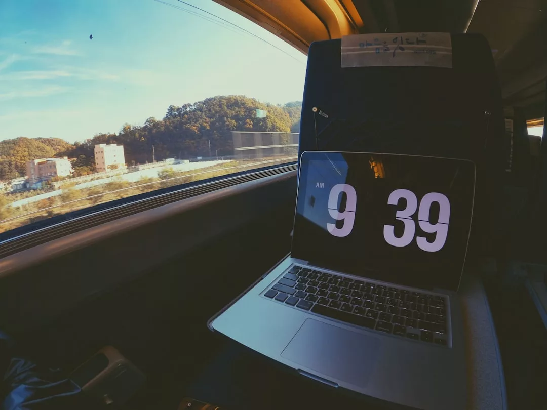 Ein Laptop, der die Uhrzeit 9:39 anzeigt, sitzt auf einem ausklappbaren Tablett in einem Zug, mit Blick auf Bäume und Gebäude draußen - perfekt für Reisen oder um Reisetipps zu notieren, besonders wenn du heiße Klimazonen erkundest.