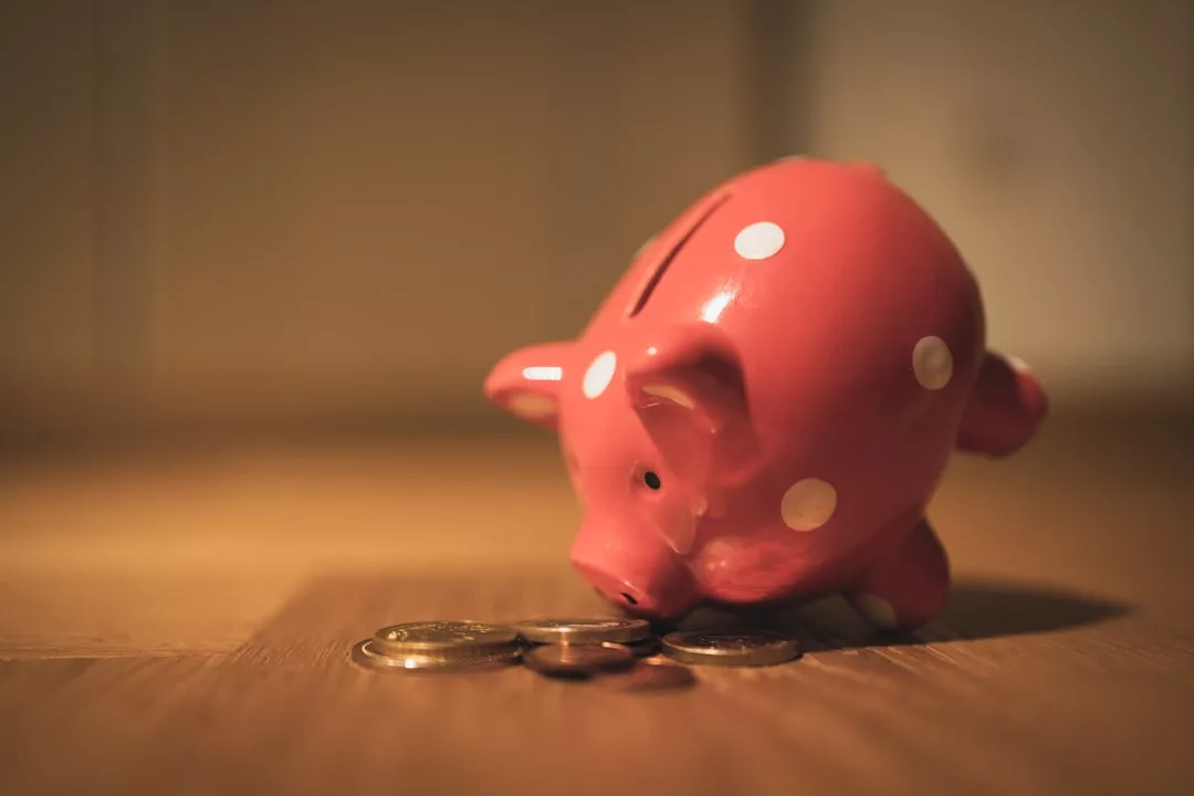 Ein rosa gepunktetes Sparschwein wird auf einer hölzernen Fläche umgedreht und mit Münzen bestreut, die den ersten Schritt zum erfolgreichen Investieren in Aktien symbolisieren.