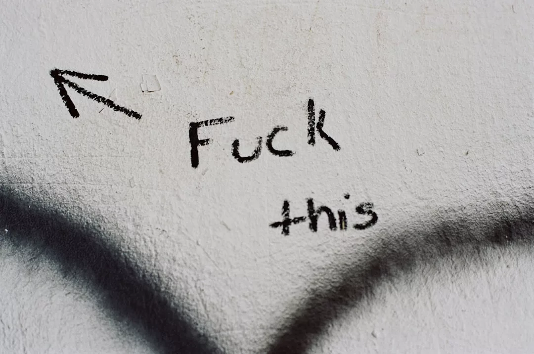 Das Graffiti auf einer weißen Wand lautet "Fuck this" mit einem Pfeil über den Worten - eine kühne Aussage, die zur Kunstanalyse einlädt und die Betrachter dazu ermutigt, Kunst kritisch zu betrachten.
